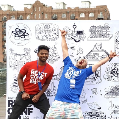 Two Thinkmill team members posing excitedly in front of the ReactConf AU banner